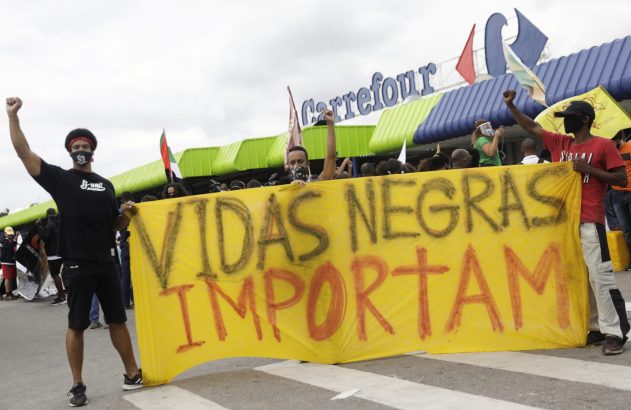 Manifestantes, alguns com punhos erguidos, seguram faixa "Vidas Negras Importam" em frente ao Carrefour.