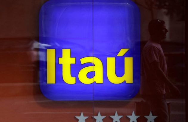 Letreiro azul-e-amarelo do Itaú em uma vitrine, com silhueta de pessoa e cinco estrelas brancas.