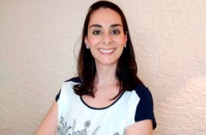 Mulher sorrindo para a câmera, com cabelo escuro e blusa clara.