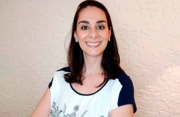 Mulher sorrindo para a câmera, com cabelo escuro e blusa clara.