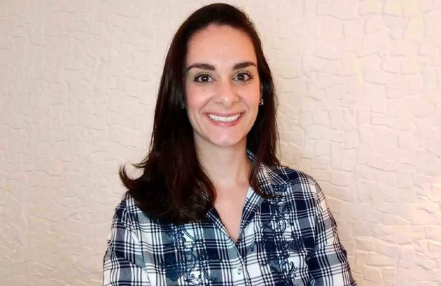 Retrato de mulher jovem sorrindo, olhando para a câmera, com camisa xadrez.