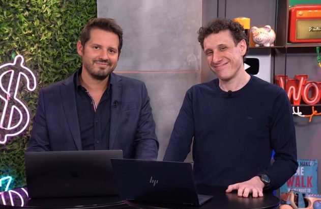 Dois homens sorrindo em estúdio com laptops à frente.