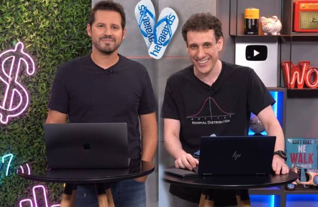 Dois homens sorridentes apresentam em estúdio com laptops, ao lado de decoração neon e chinelos Havaianas.