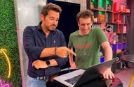 Dois homens olham para um laptop; um aponta e o outro sorri em um estúdio decorado.