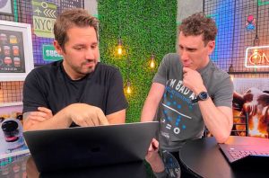 Dois homens olhando e interagindo com um laptop. Um aponta para a tela, o outro observa.