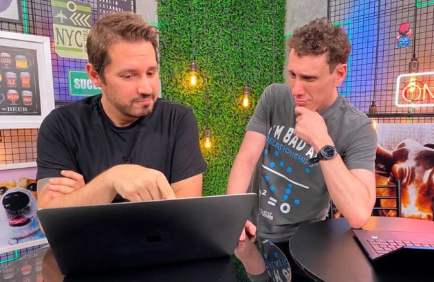 Dois homens olhando e interagindo com um laptop. Um aponta para a tela, o outro observa.