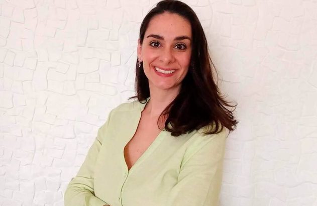 Mulher sorrindo, blusa verde, braços cruzados.