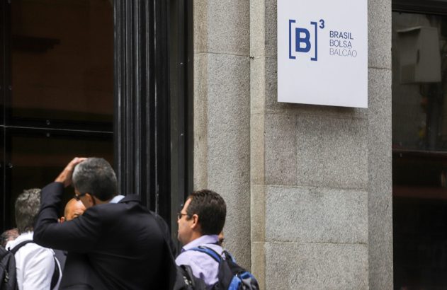 Placa "B3 Brasil Bolsa Balcão" em prédio de pedra, com homens próximos à entrada.