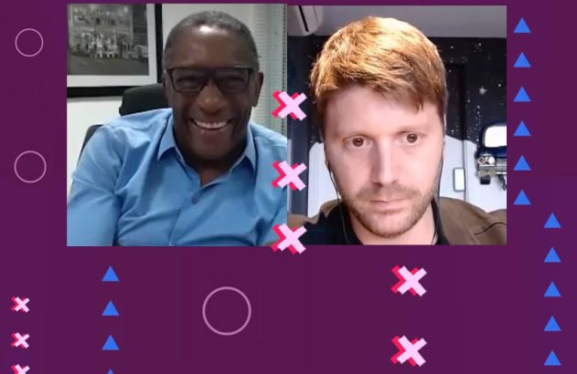 Videochamada de dois homens. O da esquerda sorri, o da direita tem expressão séria. Fundo roxo com formas geométricas.
