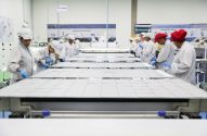 Trabalhadores montando painéis solares em linha de produção de fábrica.