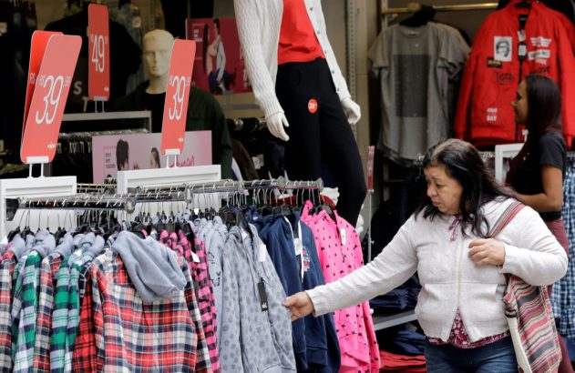 Mulher em loja de roupas examina moletons e camisas em arara. Preços R$39,99 e R$49 visíveis.