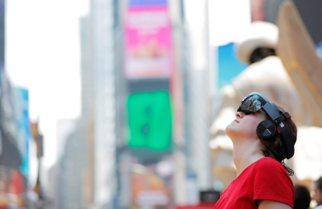 Mulher usando headset e fones de ouvido, olhando para o alto em área urbana com outdoors.