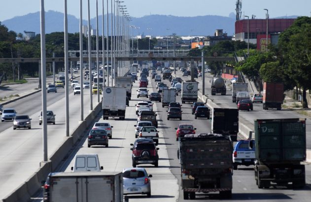 Rodovia movimentada de múltiplas faixas com tráfego intenso de carros e caminhões em um dia claro.