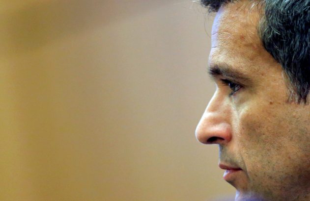 Close-up do perfil de um homem olhando para a esquerda, com fundo bege desfocado.