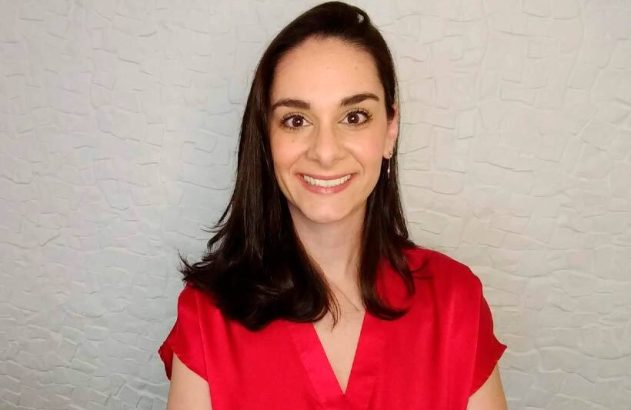 Mulher sorrindo com cabelo escuro e blusa vermelha, olhando para a câmera.