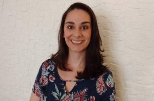 Retrato de mulher sorrindo, com cabelo escuro e blusa estampada, olhando diretamente para a câmera.