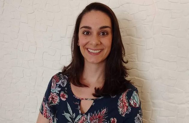 Retrato de mulher sorrindo, com cabelo escuro e blusa estampada, olhando diretamente para a câmera.