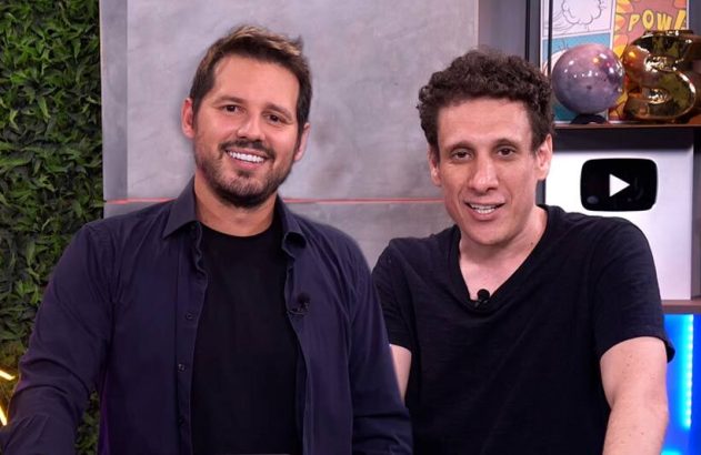 Dois homens sorrindo lado a lado em um estúdio.