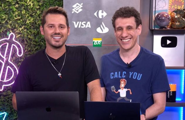 Dois homens sorrindo para a câmera, sentados com laptops. Ao fundo, um painel com logos de empresas.