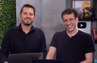 Dois homens apresentando em um estúdio de vídeo. Um sorri, o outro ri abertamente.