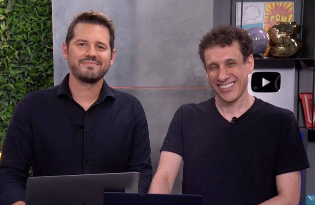 Dois homens apresentando em um estúdio de vídeo. Um sorri, o outro ri abertamente.