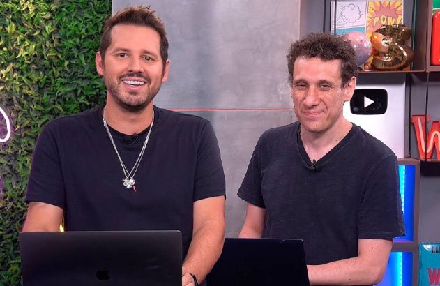 Dois homens sorridentes em estúdio, com notebooks, olhando para a câmera.