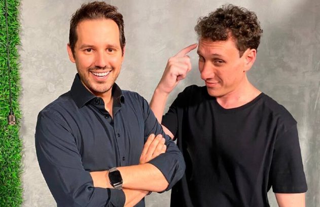 Dois homens. Um sorri com braços cruzados. O outro aponta para a própria cabeça em gesto pensativo.