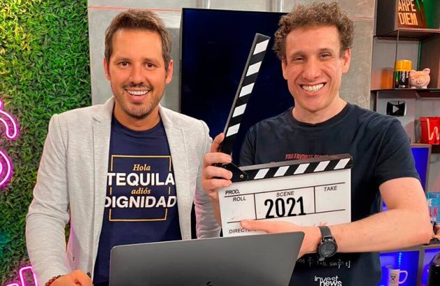 Dois homens sorridentes posam em estúdio. Um segura claquete de cinema exibindo '2021'.
