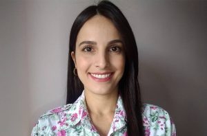 Mulher sorrindo e olhando para a câmera. Cabelo escuro, blusa estampada.