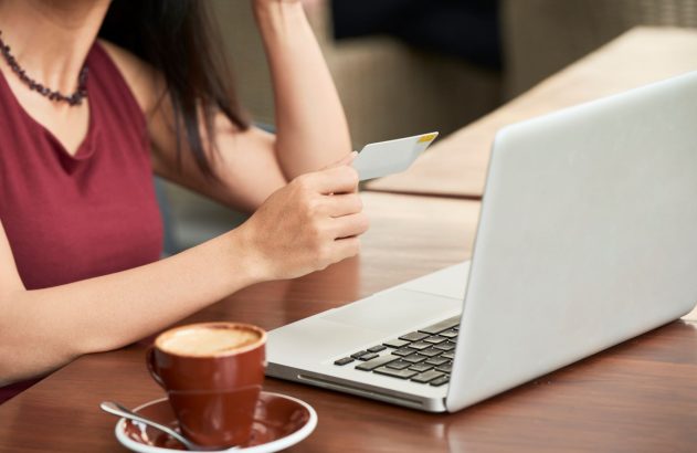 Mulher com cartão de crédito, laptop e café na mesa, fazendo compra online.