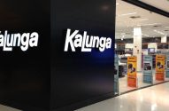 Entrada da loja Kalunga com letreiro branco iluminado e interior visível com expositores de produtos.