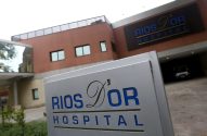 Fachada moderna do Hospital Rios D'Or, com o nome visível em letreiro e placa. Um carro estacionado na entrada.