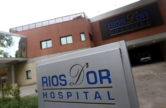 Fachada moderna do Hospital Rios D'Or, com o nome visível em letreiro e placa. Um carro estacionado na entrada.