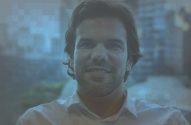 Homem sorridente com barba e camisa branca, olhando para a câmera.