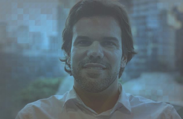 Homem sorridente com barba e camisa branca, olhando para a câmera.