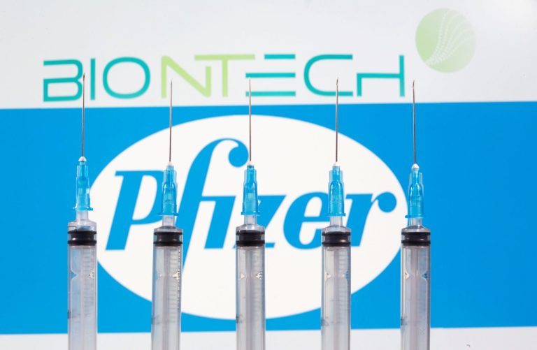 Cinco seringas com agulhas em frente aos logos BioNTech e Pfizer.