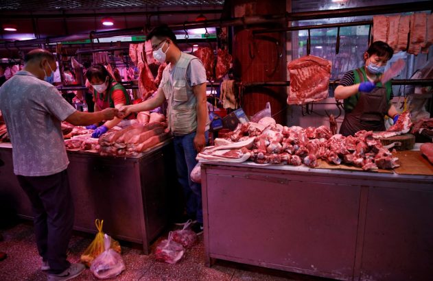 Açougueiros e clientes em mercado de carnes. Um cliente compra, outro açougueiro corta. Todos usam máscaras.