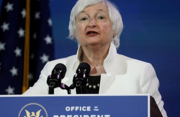 Janet Yellen discursando em um pódio com a inscrição 'Office of the President Elect' e uma bandeira dos EUA.