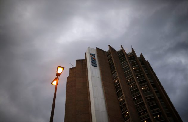 Edifício da Caixa com letreiro azul e poste de luz aceso contra um céu cinzento e nublado.