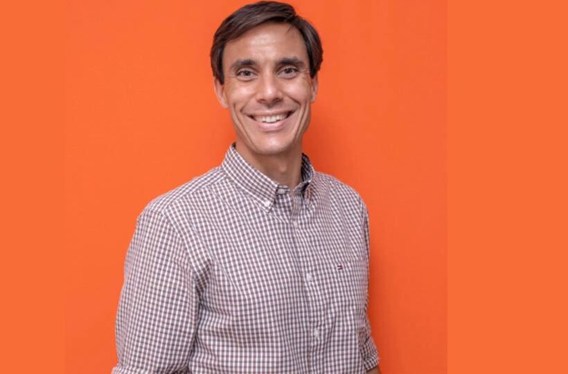 Homem sorridente de camisa xadrez em fundo laranja.