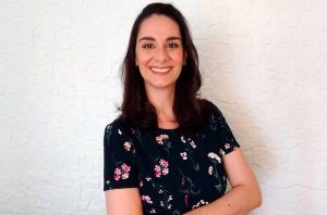 Retrato de mulher sorridente com cabelo escuro e vestido floral. Fundo branco texturizado.