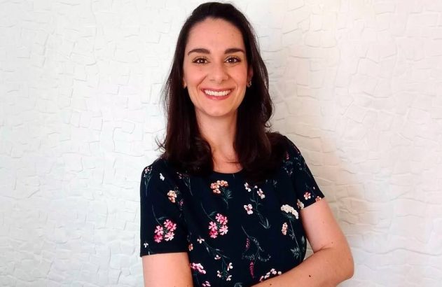 Retrato de mulher sorridente com cabelo escuro e vestido floral. Fundo branco texturizado.