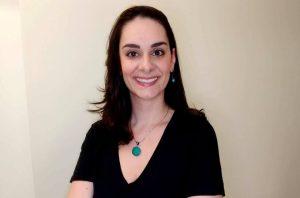 Retrato de mulher sorrindo, cabelo escuro, blusa preta e colar turquesa.