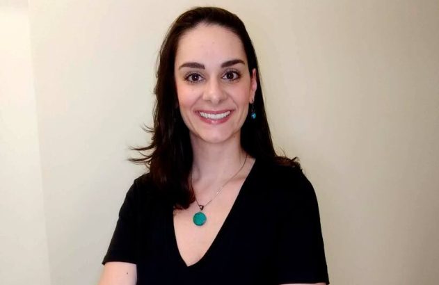 Retrato de mulher sorrindo, cabelo escuro, blusa preta e colar turquesa.