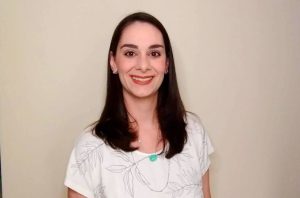 Mulher de cabelo escuro e blusa clara sorrindo para a câmera.