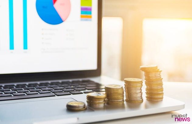 Laptop com gráficos financeiros e pilhas de moedas crescendo, simbolizando investimento e crescimento. (88 caracteres)