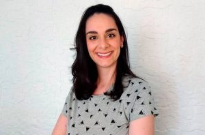 Mulher sorrindo com cabelo escuro e camisa estampada contra fundo branco.