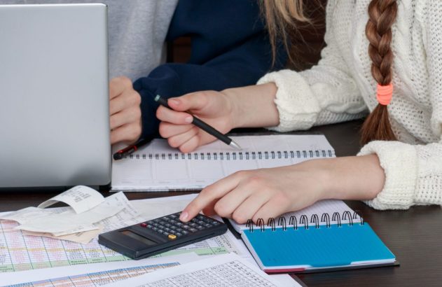 Pessoas analisando documentos financeiros em uma mesa com calculadora e laptop.