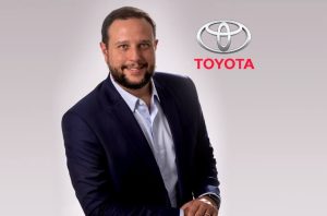 Executivo sorrindo em terno, com logo da Toyota.