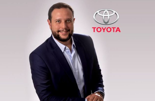 Executivo sorrindo em terno, com logo da Toyota.